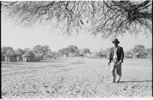 Man standing, with view of huts and buildings of Tsau in background