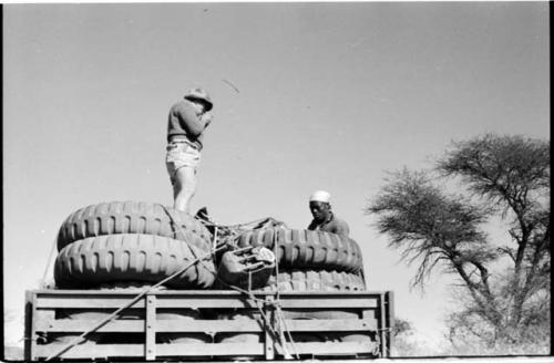 Simon Molamo and Casper Kruger sitting and standing on top of GMC tires on the top of an expedition truck