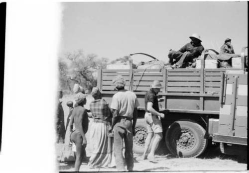 Group of people standing around expedition truck, men sitting inside truck (image partly obscured)