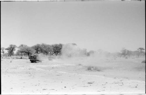 Expedition trucks crossing bare ground, with sand blowing