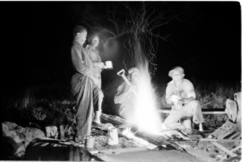 Expedition staff standing and sitting by a fire a night