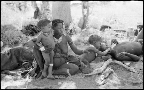 Debe standing by his mother holding mealies, and /Gaishay giving "≠Gao Lame" a bite of mealies