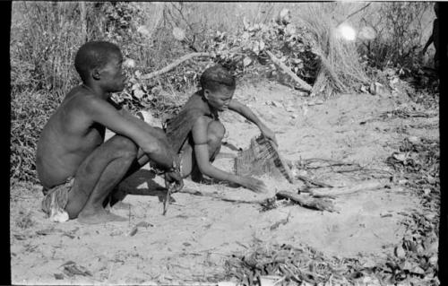 Tsekue sifting roasted tsama melon seeds from ashes, !Gai sitting beside her