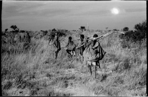 Group of people returning from gathering tsama melons; /Twikwe carrying a log of wood