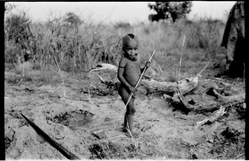 N!whakwe standing holding a stick