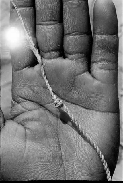 Person's hand holding up cord with a knot, close-up