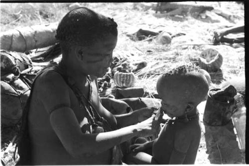 Tsekue giving N!whakwe a piece of meat, cutting it off at his lips with a knife