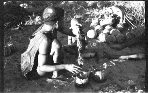 Tsekue holding tsama melon pulp, N!whakwe sitting beside her