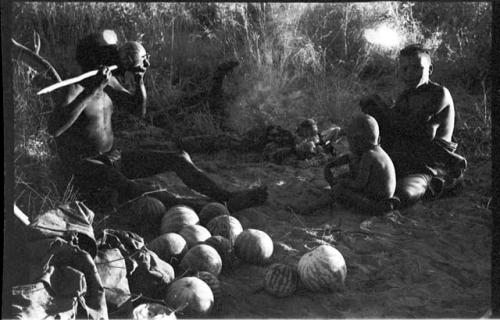 !Gai sitting eating from a tsama melon. Tsekue and N!whakwe sitting beside him