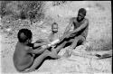 !Gai and //Kwaiǂkabe stripping bark from root for making a quiver, N!whakwe sitting beside !Gai