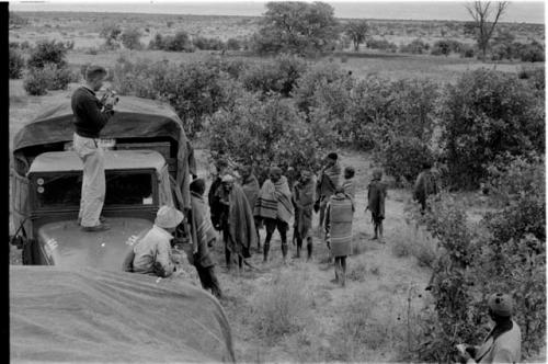 Group standing by expedition truck, two expedition members on top of truck