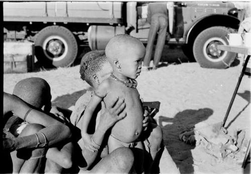 N!whakwe and Tsekue sitting with /Twikwe and !Oukabe, expedition truck in background