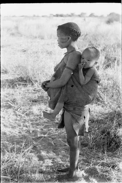 Tsekue carrying N!whakwe on her back, side view