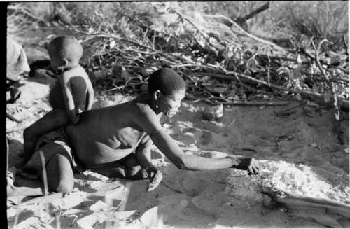 /Twikwe getting a coal to light her pipe, N!whakwe sitting on her back