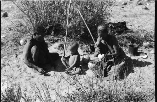 Oukwane and //Kuǂtera sitting beside their fire, N!whakwe sitting with them