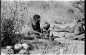 Oukwane sitting with N!whakwe beside him drinking from a tin can