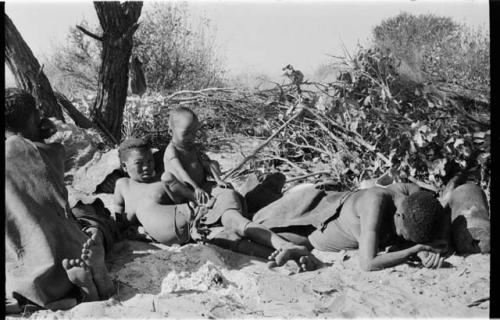 /Twikwe, DaSi!Na and Tsekue reclining, and N!whakwe sitting on top of Tsekue