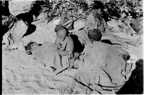 /Twikwe, DaSi!Na and Tsekue reclining, and N!whakwe sitting on top of Tsekue