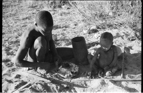 !Gai cutting into a turle with a paddle, N!whakwe sitting beside him