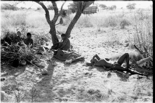 !Gai lying on ground, Tsekue lying under a blanket; /Twikwe, DaSi!Na and N!whakwe sitting nearby