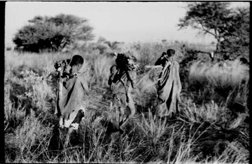 Tsekue carrying N!whakwe and two women coming into the werft, with wood on their shoulders