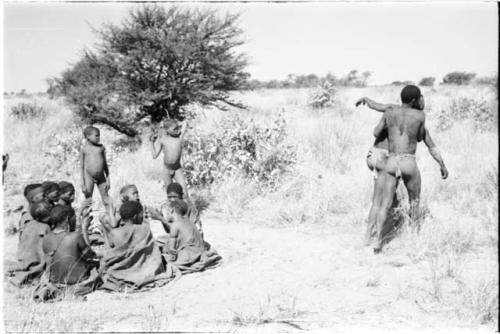 Group of people watching a medicine man walking off assisted by another man