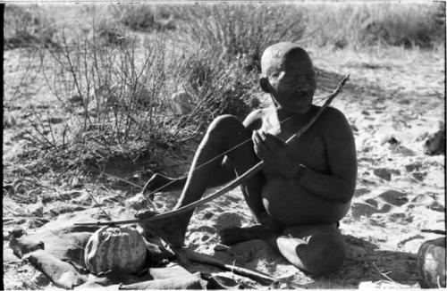 Oukwane playing a musical bow, seated