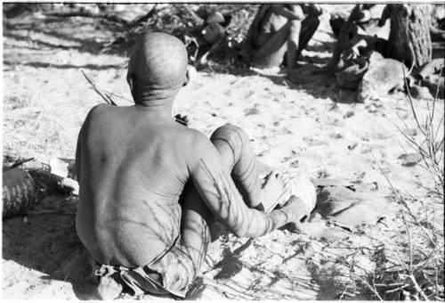 Oukwane seated and playing a musical bow, seen from behind