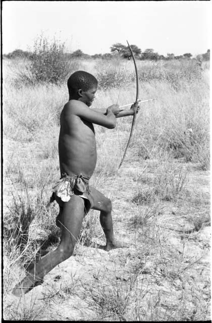 !Gai demonstrating shooting an arrow, seen from behind, full figure standing