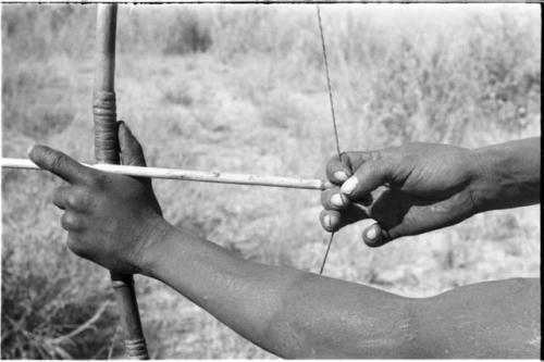 Close-up of !Gai's hands shooting an arrow