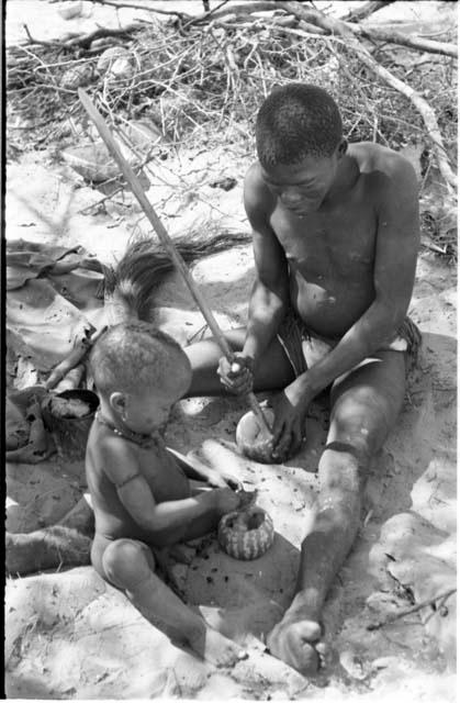 !Gai and N!whakwe with tsama melons sitting at their place in the werft