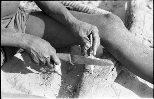 Close-up of !Gai's hands shaping an arrow point made of bone