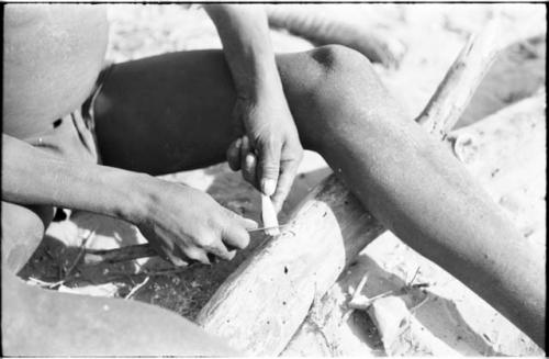 Close-up of !Gai's hands, shown sharpening a piece of bone