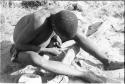 !Gai sharpening a piece of bone, full seated figure