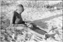 !Oukabe seated playing a sanza placed on empty melon rind used as a sounding board