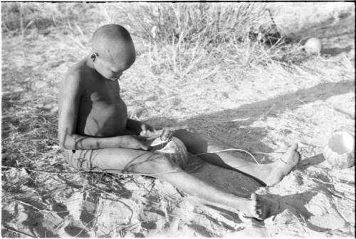 !Oukabe seated playing a sanza placed on empty melon rind used as a sounding board