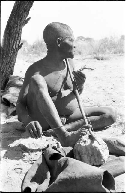 Oukwane seated, playing a bow