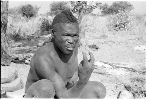 Visiting man demonstrating hunting hand signals, half figure seated