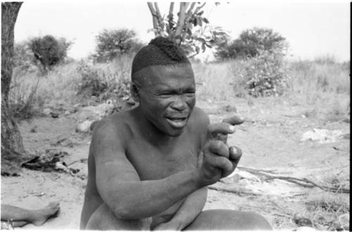 Visiting man demonstrating hunting hand signals, half figure seated