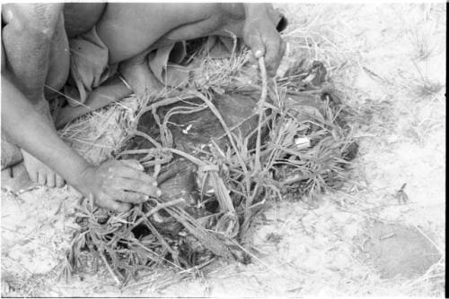 Close-up of  !Gai's hands tying up a carrying net