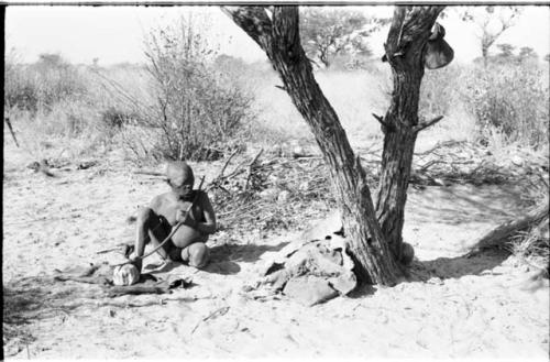 Oukwane seated, playing a bow under a tree