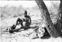 Oukwane seated, playing a bow under a tree