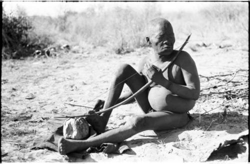 Oukwane seated, playing a bow under a tree