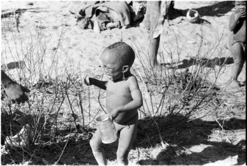 N!whakwe crying, holding a small turtle and a tin in his hands