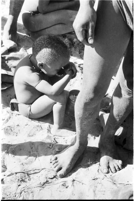 N!whakwe crouched holding a turtle near his mouth