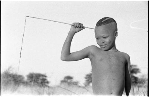 Boy holding a stick, to which a feather is attached by a thong, to make a noise