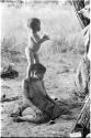 N!whakwe standing on his mother Tsekue's shoulder to look over the grass to see what was making noise