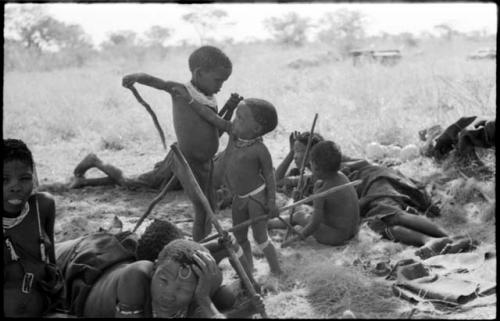 "The visiting girl" sitting, !U lying down with Norna against her, Di!ai's sons /Gaishay and Debe playing with sticks, and Bau sitting with /Naoka (Di!ai's co-wife)