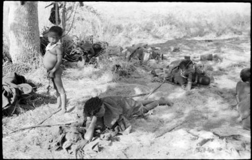 Group of people resting under a tree, including //Khuga, Bau, Di!ai and /Naoka, and Di!ai's son /Gaishay standing