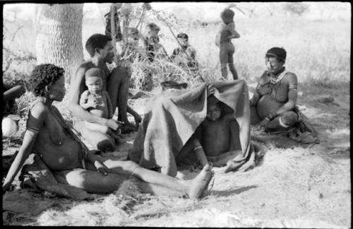 Group of children under a kaross, Debe sitting in his father's lap, and /Naoka and Di!ai sitting